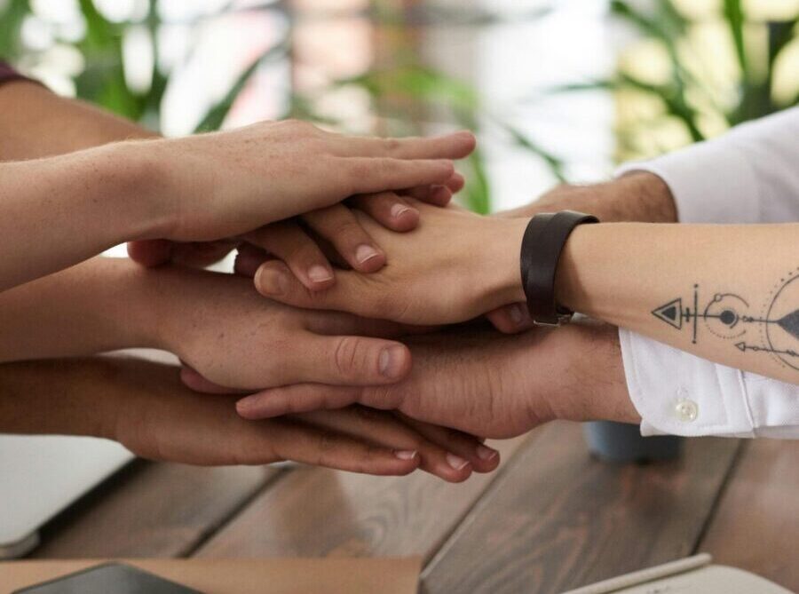 Hands from a diverse team stack on a table symbolizing unity and teamwork in a modern office setting.