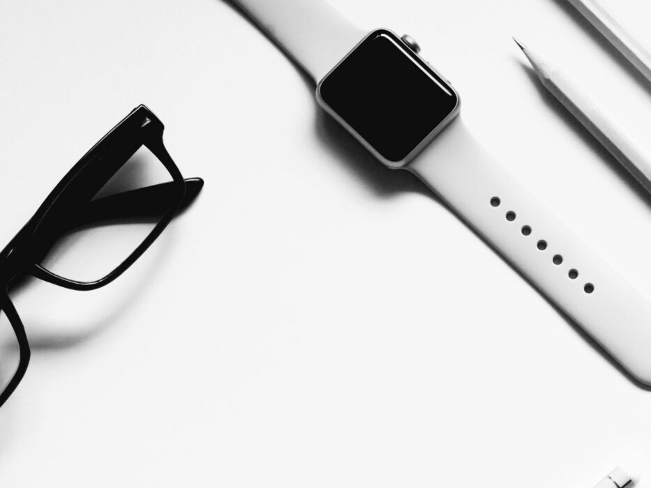 A sleek black-and-white flat lay of a modern office desk featuring a smartwatch and glasses.